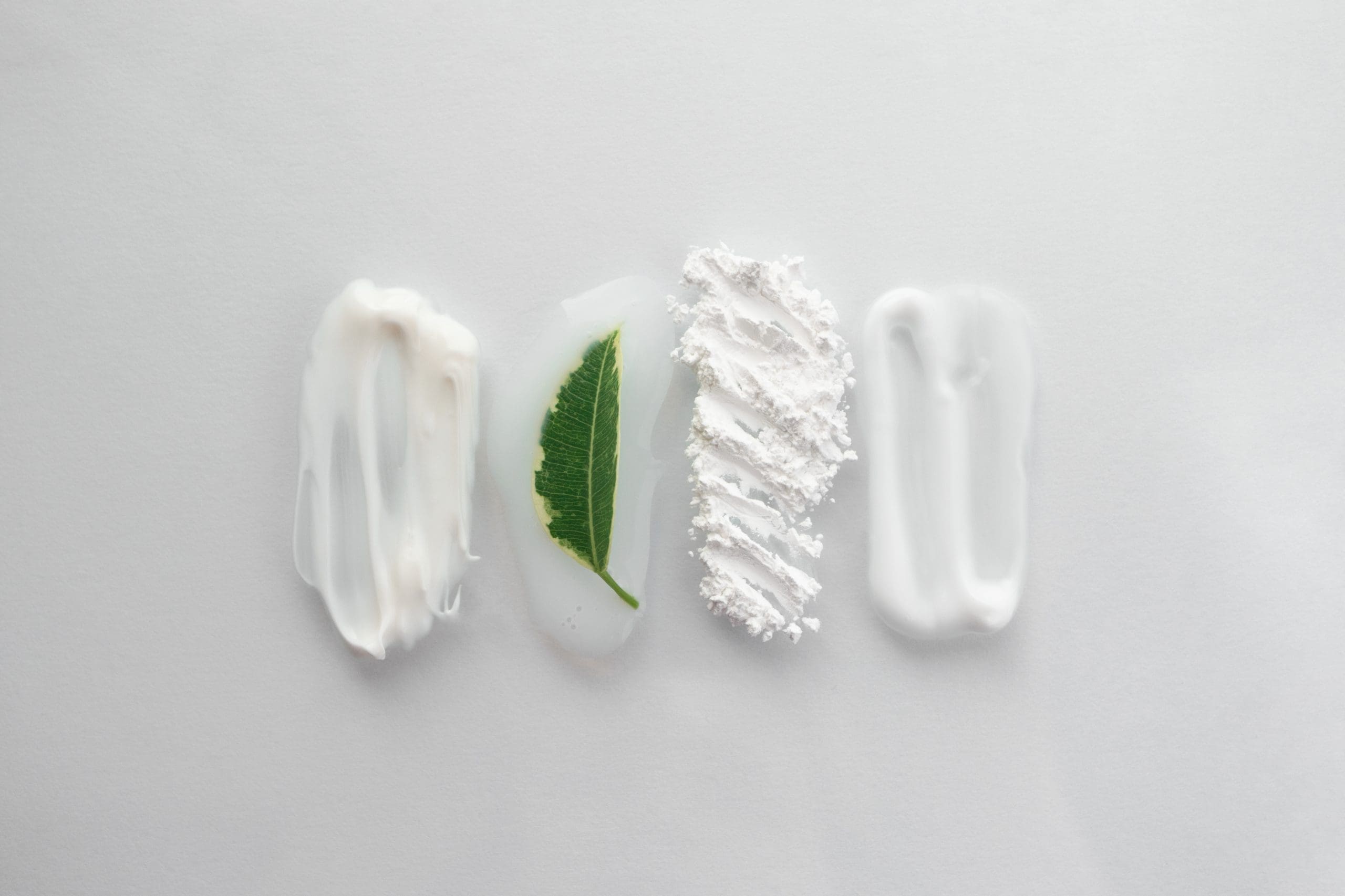 Four skincare swatches in a row: cream, clear gel with a green leaf, white powder and lotion