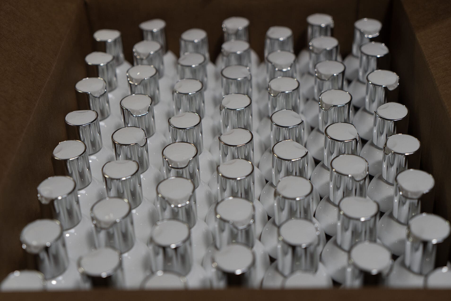 Shipping case filled with white bottles with silver caps, seen from above