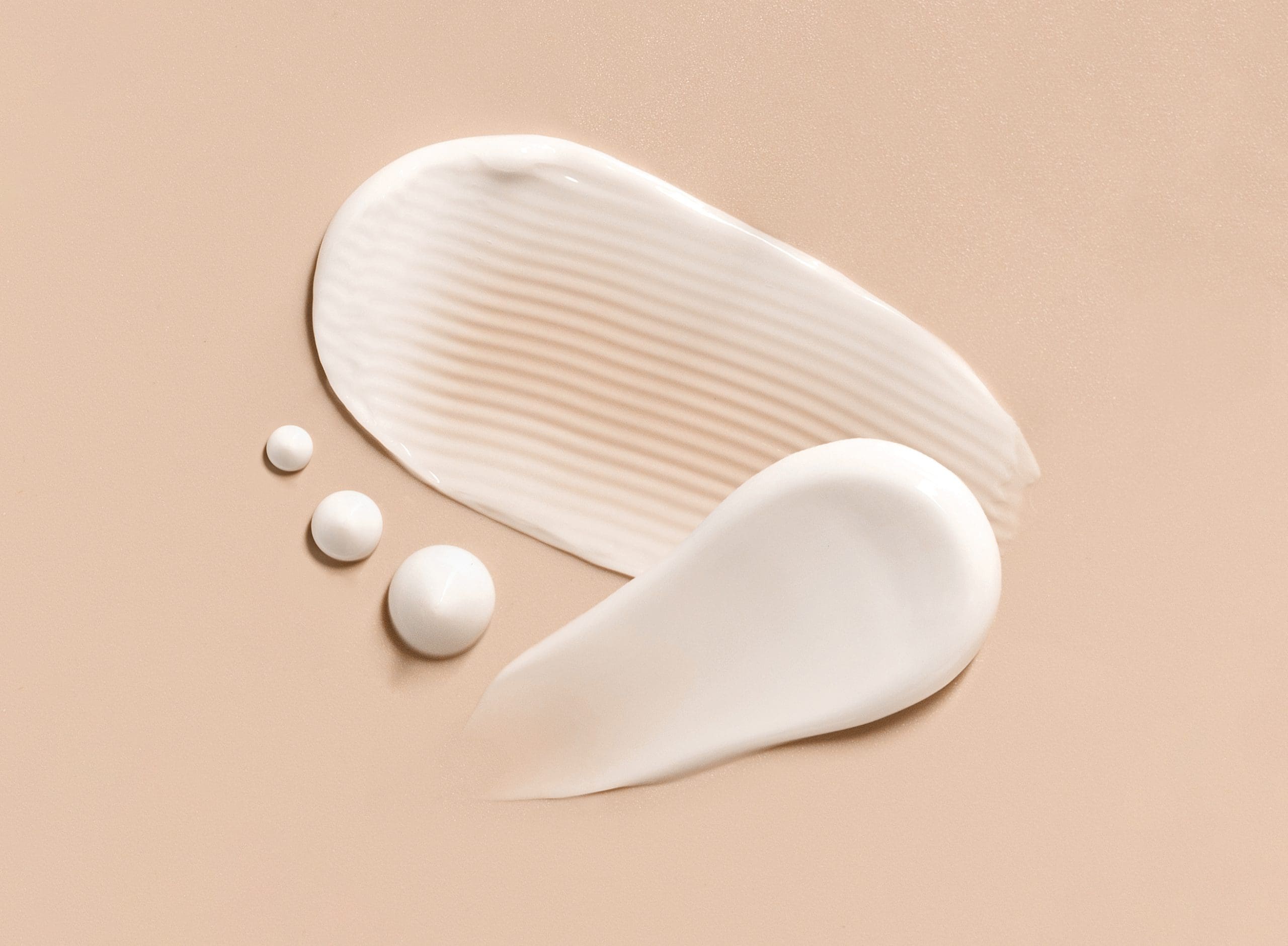 Smears of white cream and lotion with small droplets on a peach background