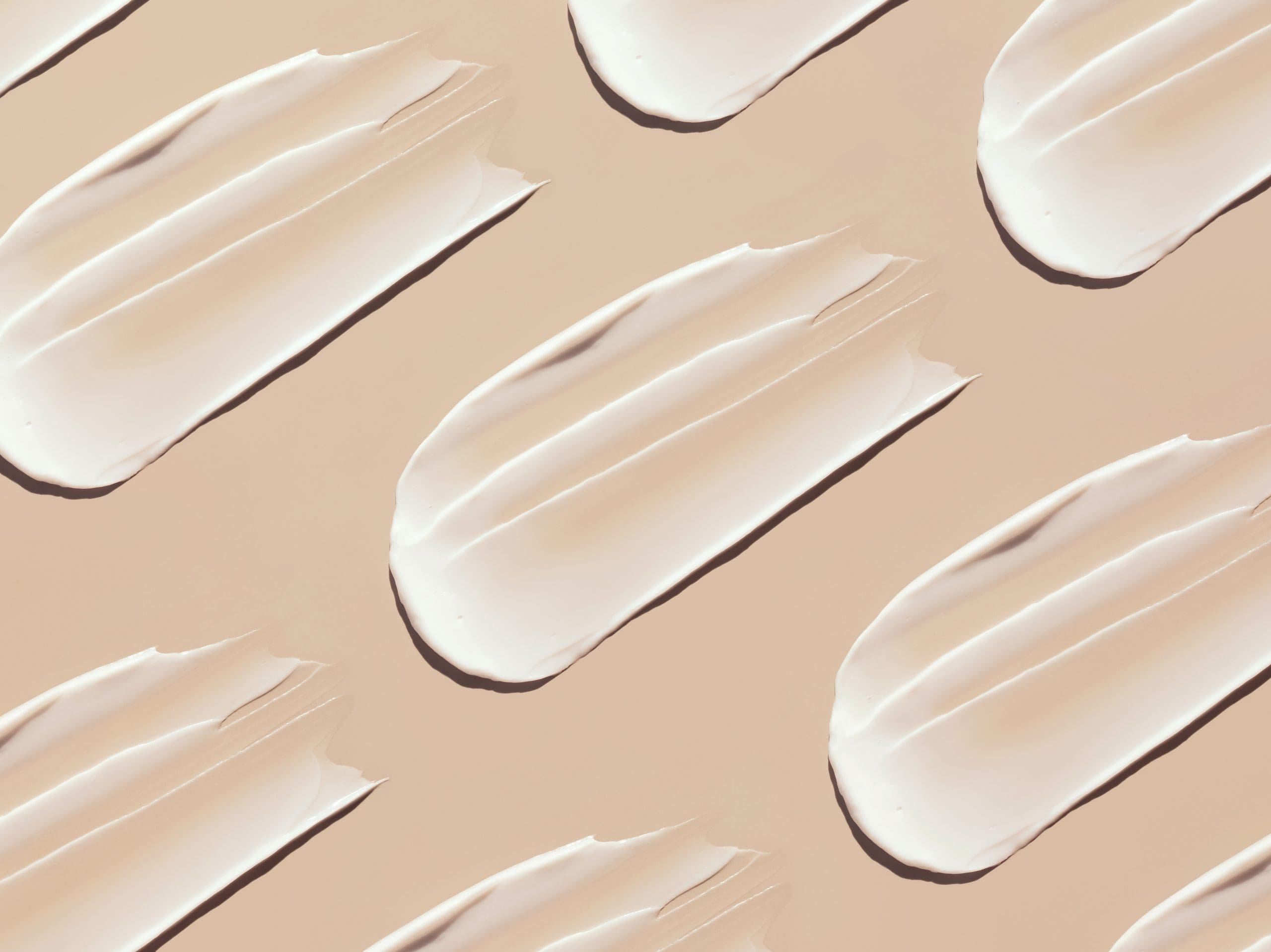 Diagonal swatches of white lotion on a peach background
